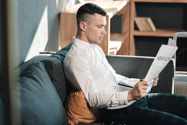 Jovem empresário bonito sentado no sofá leitura jornal — Fotografia de Stock