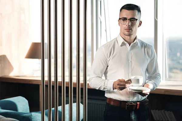 Стильний молодий економіст стоїть біля вікна п'є ранкову каву — стокове фото