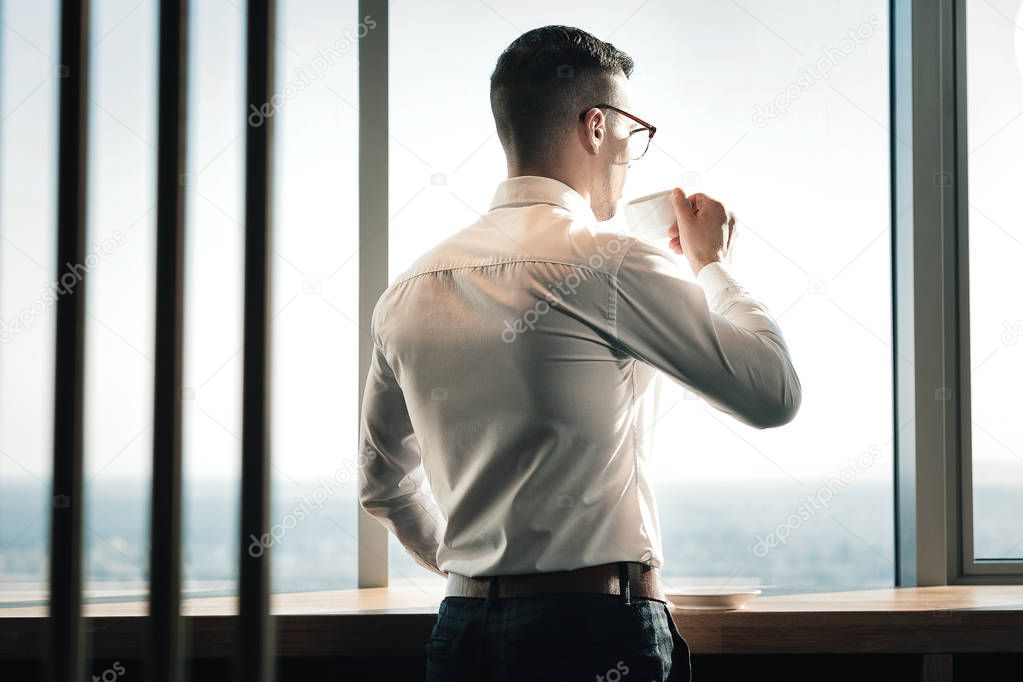 Young stylish economist standing and looking into the window