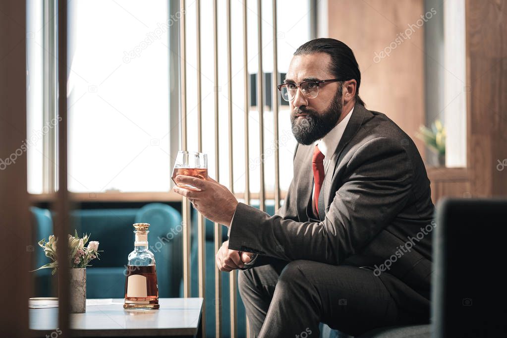 Bearded businessman wearing red tie holding glass of cognac