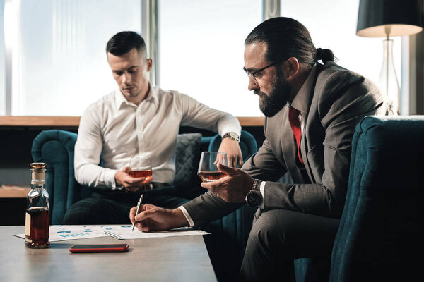 Two business partners drinking whisky and filling the documents