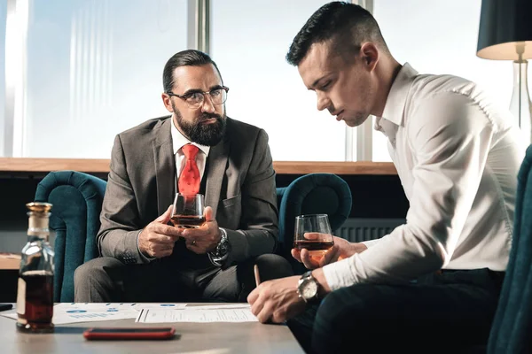 Jefe viendo a su joven aprendiz trabajando y bebiendo whisky — Foto de Stock