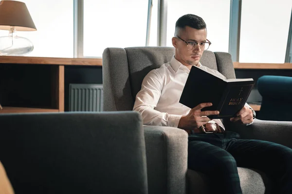 Kluger junger Mann mit Brille beim Lesen der Heiligen Bibel — Stockfoto