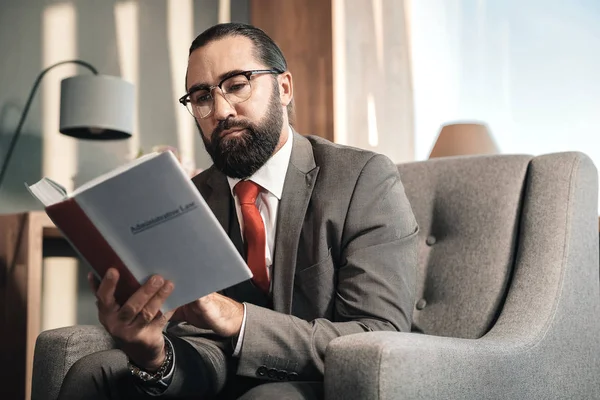 Bärtiger smarter Anwalt mit roter Krawatte liest Verwaltungsrecht — Stockfoto