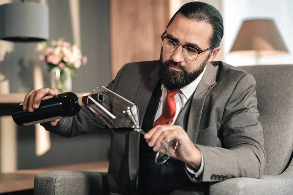 Hombre con gafas y corbata roja vertiendo vino tinto en su copa — Foto de Stock