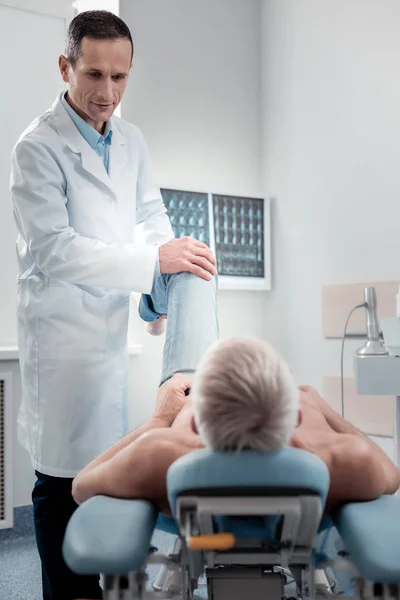 Ernsthafter Arzt überprüft ausgekugeltes Knie — Stockfoto