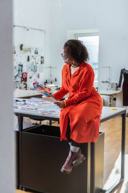 Meraklı kıvırcık tabaklanmış kadın dergileri fotoğraflardan gözlemleyerek