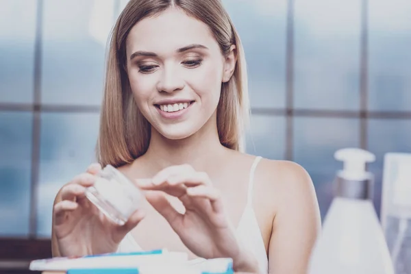 Agradable joven mujer mirando en un frasco de crema facial — Foto de Stock