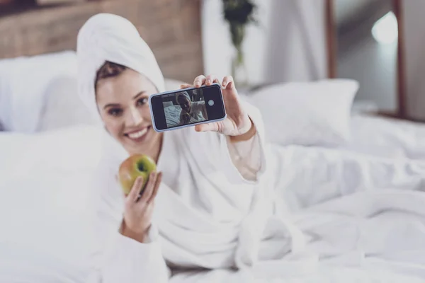 Молода жінка лежить на ліжку зі смартфоном — стокове фото