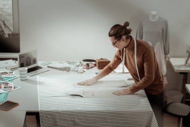 Kumaş kesme için hazırlanıyor kahverengi bir giysi içinde uzun boylu profesyonel tasarımcı