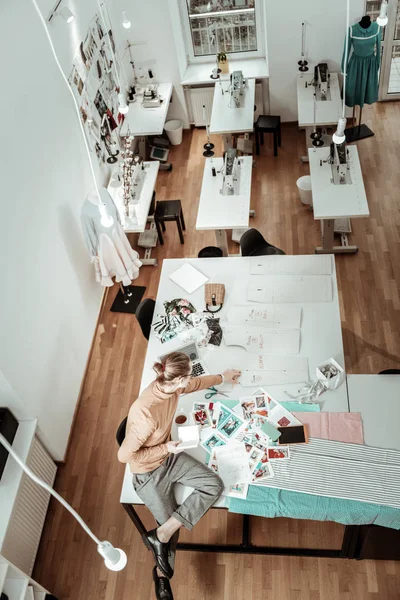 Diseñador alto de pelo rubio en una prenda marrón mirando a través de nuevos bocetos — Foto de Stock