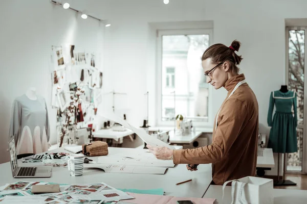 Fair-haired tall designer in a brown garment working on a new dress