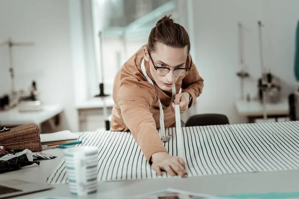 Jonge knappe ontwerper in brillen met lange haren werken met textiel — Stockfoto