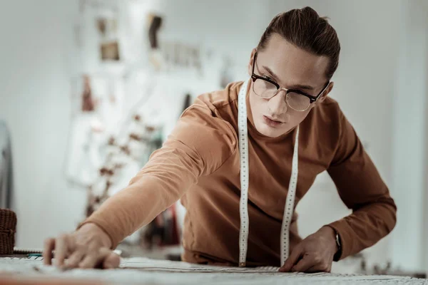 Jonge langharige professionele ontwerper in een bruin kledingstuk werken met stof — Stockfoto