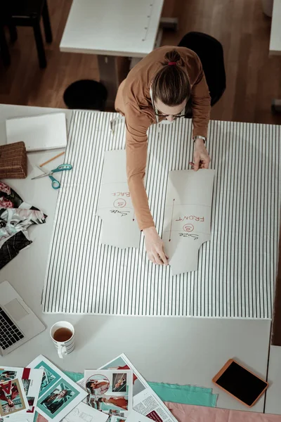 Tall fair-haired designer in a brown garment working with patterns