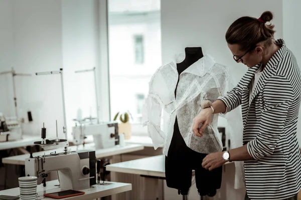 Handsome young fashion dressmaker in eyeglasses putting the blouse on a dummy
