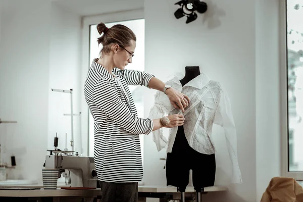Hermosa joven modista de moda en una chaqueta a rayas que mira ocupado en un taller — Foto de Stock