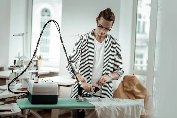 Elegante joven diseñador de moda en una chaqueta a rayas haciendo planchado — Foto de Stock