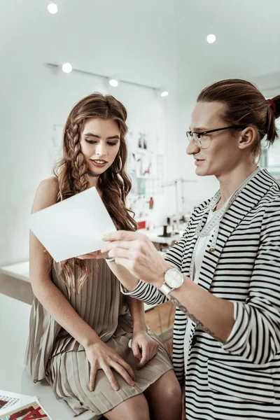 Long-haired designer in eyeglasses showing a picture to a beautiful model