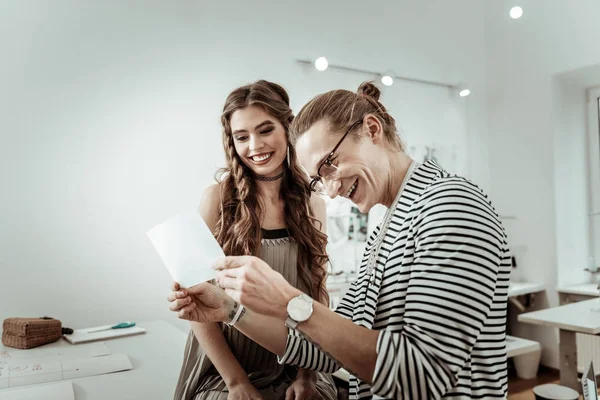 Long-haired designer in eyeglasses and a pretty model laughing at the picture
