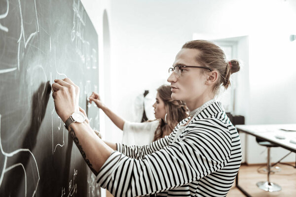 Handsome young dressmaker in eyeglasses and a beautiful model looking concentrated