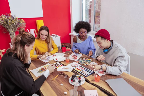 Cuatro prometedores estudiantes de arte usando pinturas mientras dibujan — Foto de Stock