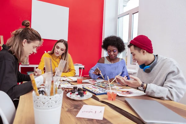 Four art students holding their painting brushes while drawing