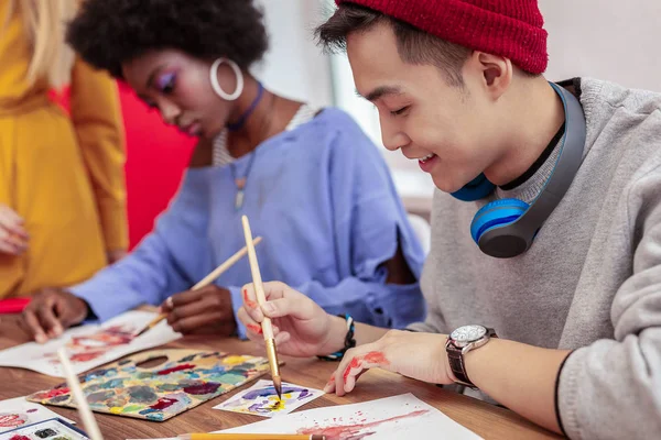 Hermoso estudiante de arte radiante con sombrero rojo sosteniendo pincel de pintura — Foto de Stock