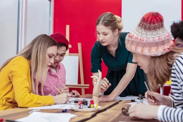 Blonde-haired team leader helping art students painting