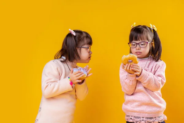 Petites filles intéressées par le syndrome du duvet observant leurs beignets — Photo