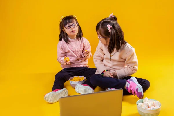 Adorable little twins sitting on bare floor with marshmallow and chips — Stock Photo, Image