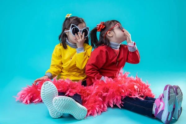 Two happy girls sitting on studio floor while wearing glasses — Stock Photo, Image