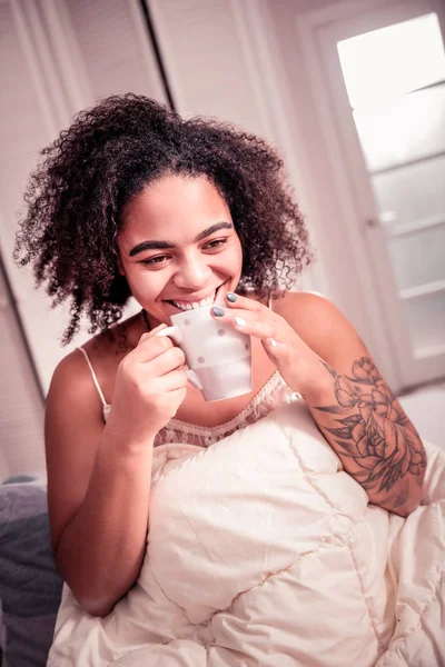 Laughing beautiful woman with thick brows having morning hot drink