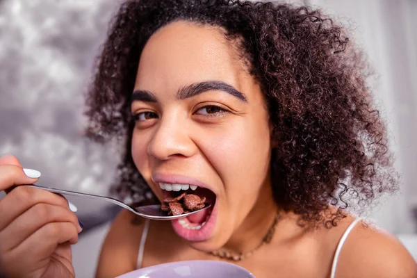 Atractiva dama morena lanzando cereales de chocolate en su boca abierta —  Fotos de Stock