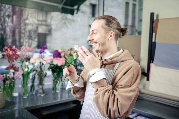 Bonito jardineiro cheirando rosa com sorriso sincero — Fotografia de Stock