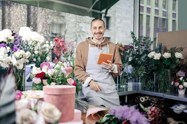 Bonito jardineiro sentado entre flores na loja — Fotografia de Stock