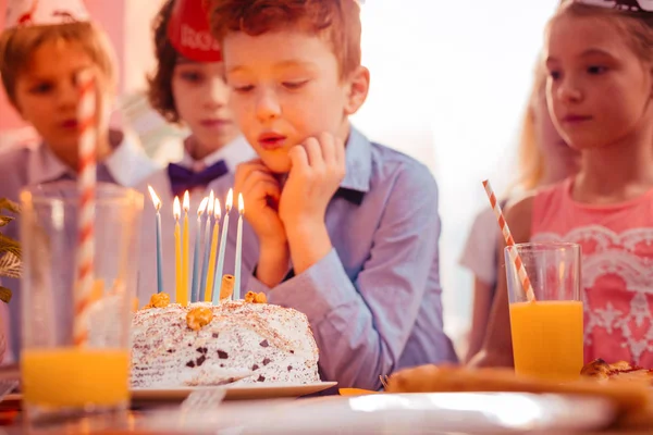 Сконцентрированный рыжий мальчик задувает свечи на торте — стоковое фото