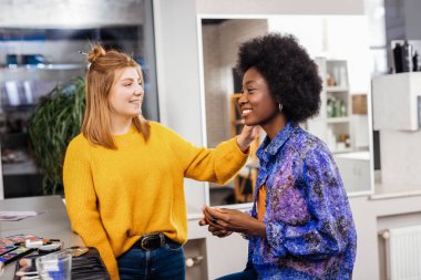 Sarışın olumlu stilist makyaj bir Afro-Amerikan modeli