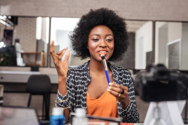 Vackra afroamerikanska kvinna med ljusa läppstift visar en ansiktsborste — Stockfoto