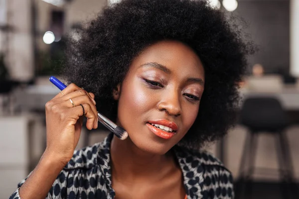 Pretty african american woman with curly hair putting a new concealer on her face — Stock Photo, Image