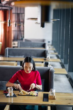 Restoranda yemek yerken çatal ve bıçak kullanan esmer kadın