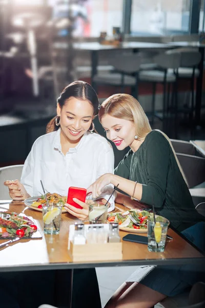 Dois melhores amigos lendo feed de notícias no smartphone vermelho durante o jantar — Fotografia de Stock