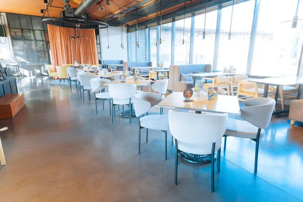 White comfy armchairs standing near wooden tables in restaurant