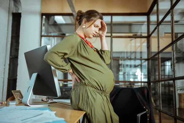 Mörkhårig gravid kvinna bär khaki klänning att ha huvudvärk — Stockfoto