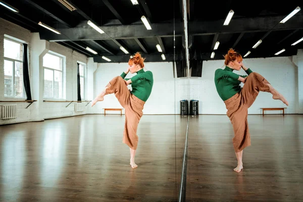 Cute red-haired professional dancer in a green turtleneck doing complicated movements