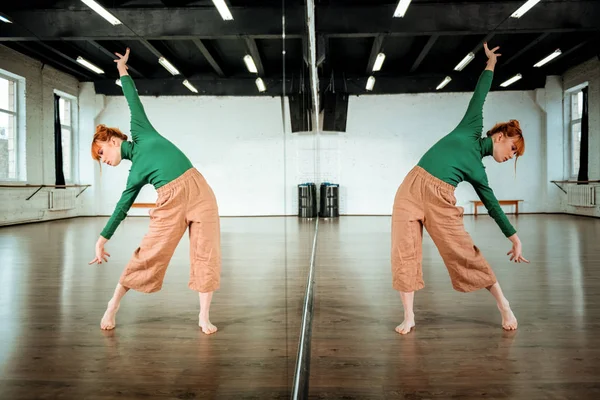 Cute red-haired dance teacher in a green turtleneck doing inclinations