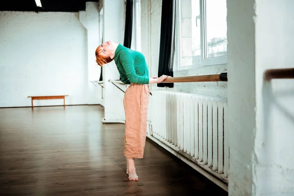 Dançarina de balé profissional ruiva com coque de cabelo em pé perto da barra de balé — Fotografia de Stock