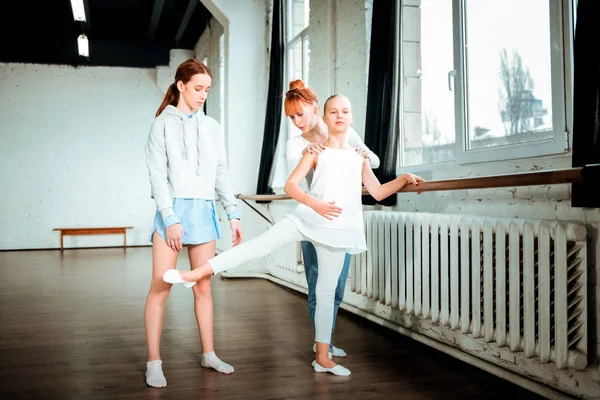 Adolescente rubia de pelo largo en ropa deportiva blanca haciendo ejercicio cerca del bar de ballet —  Fotos de Stock