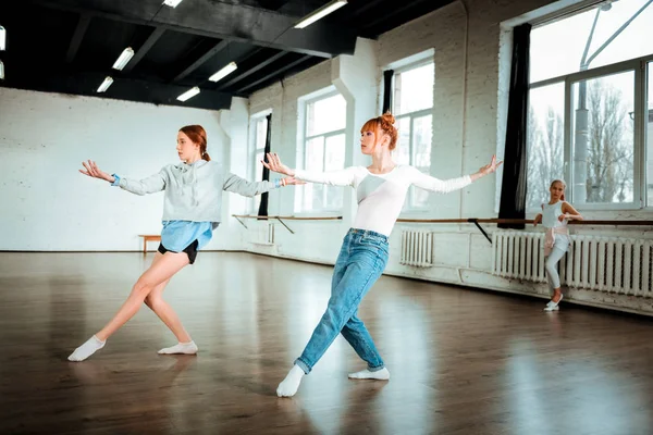 Beautiful red-haired professional dancer in blue jeans and her student dancing in the studio