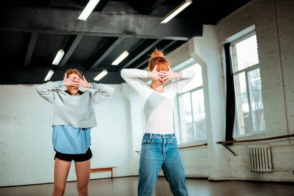 Beautiful red-haired teacher in blue jeans and a student in black shorts spending time in a dance studio
